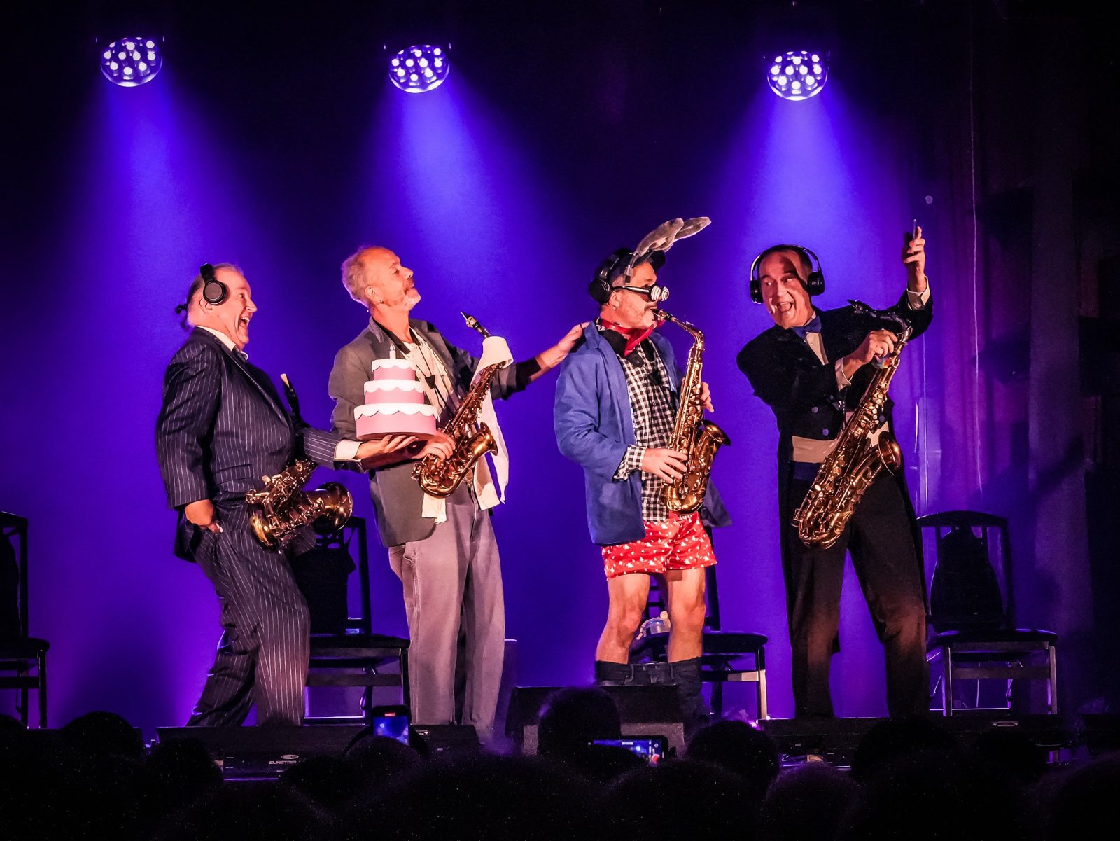 Quatre saxophonistes en costume sur scène sous une lumière violette